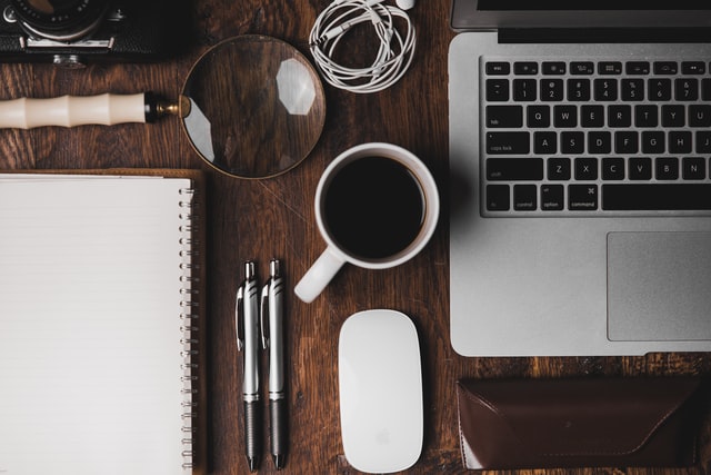 a desk with a laptop, cup of coffee, mouse, and other creative tools