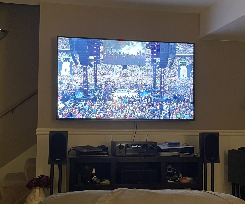 A cluttered home theater with a receiver, two speakers, a PS4, and a PS5 on a TV stand.