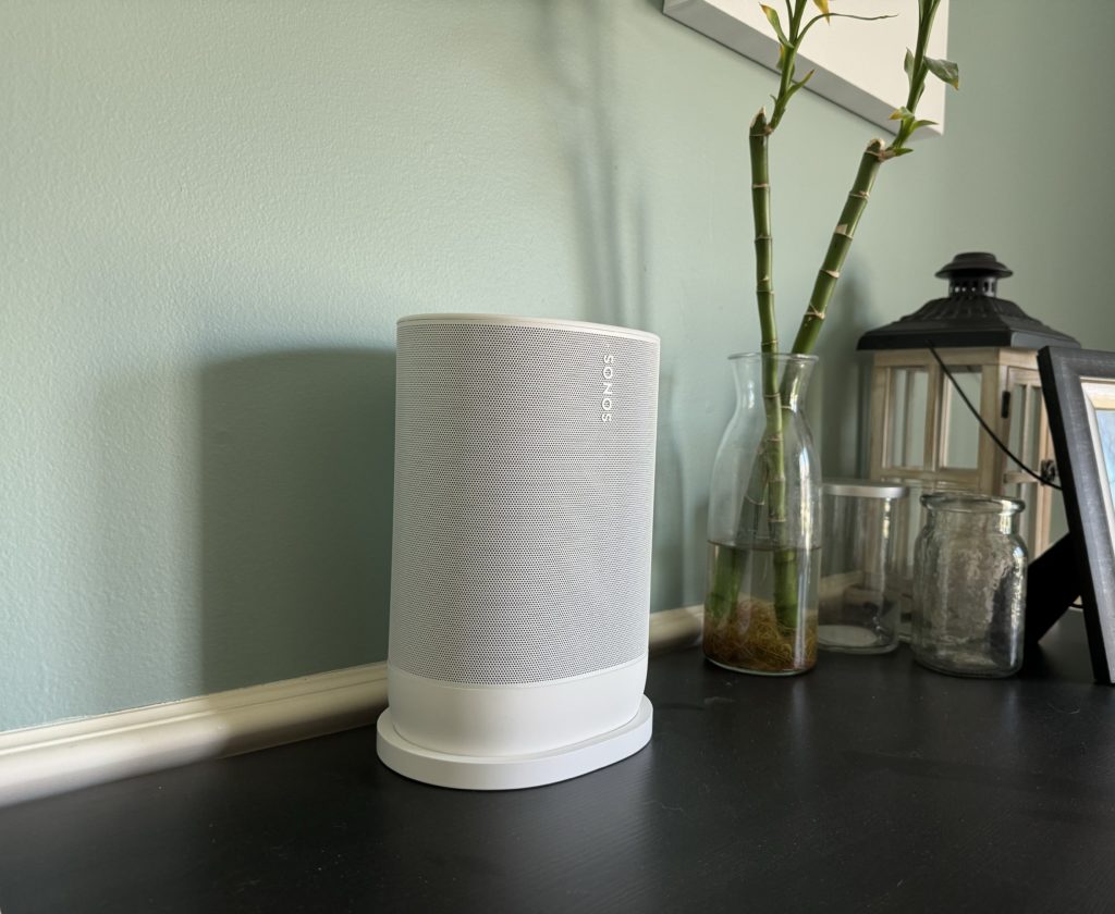 A white Sonos Move 2 on a dark table. A bamboo plant is in the background.